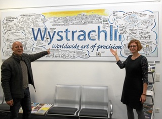 Anne Reiter (Leiterin der Unternehmenskommunikation, Firma Wystrach) und Khalid Rashid (vom Büro für Kultur und Tourismus der Gemeinde Weeze) freuen sich über die pfiffige Grafik, die Weeze protokolliert und zur Schau im Rathaus ausgestellt ist. 
