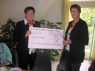 Astrid Hölsken, Sparkasse Weeze, links im Bild, übergibt den Scheck an Hanni van Hall, Vorsitzende des Krankenbesuchsdienstes