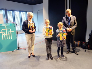 Regierungspräsidentin Birgitta Rademacher (links im Bild) und Gouverneur Theo Bovens überreichen gemeinsam die ersten Exemplare des Mitmachbuches an die Schülerinnen Lisa van Asten (2. von links im Bild) und Carlotta Scuderi